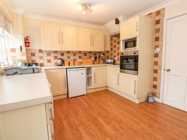 A kitchen with wooden cabinets a small fridge an oven and microwave and a tiled backsplash at The Chace in Portreath