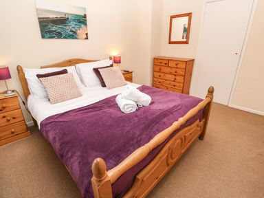 A bedroom with a wooden bed with purple blanket two nightstands lamps and a wooden dresser at The Chace in Portreath