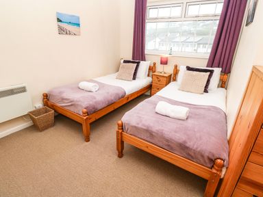 A bedroom with two single wooden beds with purple blankets and cushions a nightstand a lamp a window and a wicker basket at The Chace in Portreath