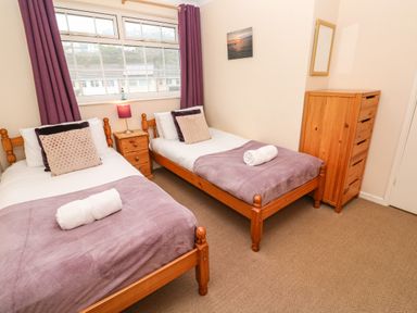 A bedroom with two single beds with purple blankets and pillows a wooden nightstand with a lamp and a wooden dresser with a mirror at The Chace in Portreath