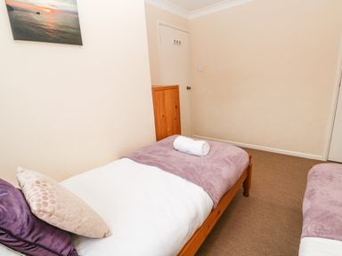 A bedroom with two single beds with purple blankets and pillows a wooden wardrobe and a wall painting at The Chace in Portreath
