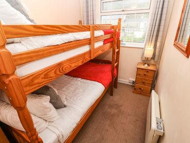 A bedroom with wooden bunk beds a window bedside table with lamp and a wall heater at The Chace in Portreath