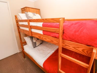 A bedroom with wooden bunk beds with red blankets two gray pillows and a wooden dresser at The Chace in Portreath