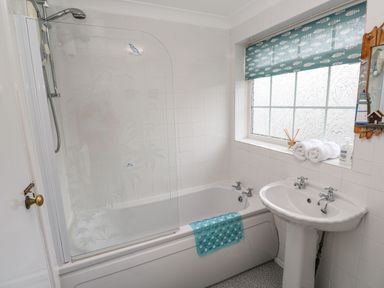 A bathroom with a bathtub shower combination a sink and a window with a fish patterned blind at The Chace in Portreath