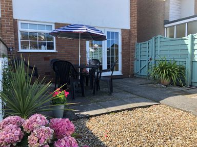 An outdoor patio with a table umbrella black chairs potted plants and a light blue fence at The Chace in Portreath