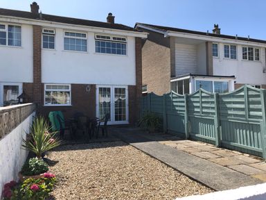 A backyard with patio furniture gravel and plants with a fence and two-story houses at The Chace in Portreath
