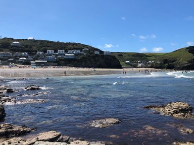 A beach with people on the sand and waves near houses on a hillside at The Chace in Portreath