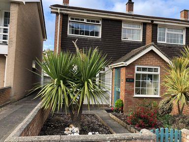 The front of a brick and wood house with plants and a blue gate at The Chace in Portreath