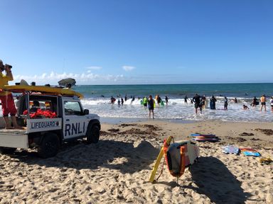 A lifeguard vehicle and equipment on a sandy beach with people swimming and playing in the sea at The Chace in Portreath