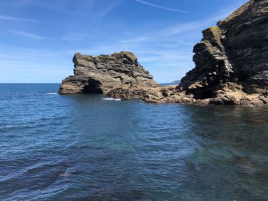 A coastal scene with rock formations and ocean water under a blue sky at The Chace in Portreath