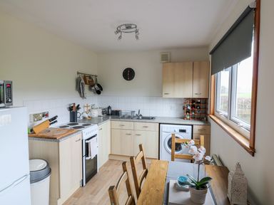 A kitchen with wooden cabinets a dining table and a window with a blind at Kestrel Lodge in Dumfries