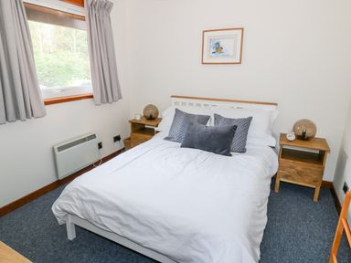 A bedroom with a bed and pillows two wooden bedside tables with lamps and a window with curtains at Kestrel Lodge in Dumfries