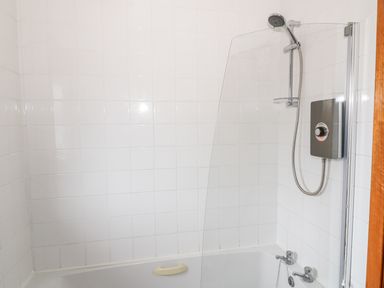 A bathroom with white tiled walls a bathtub a showerhead and a glass shower screen at Kestrel Lodge in Dumfries