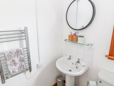 A small bathroom with a sink a round mirror a towel rail with a towel and a white toilet at Kestrel Lodge in Dumfries