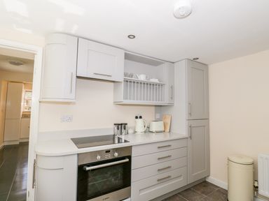 A kitchen with grey cabinets oven stovetop kettle toaster and a trash bin at Rose Cottage in Bream