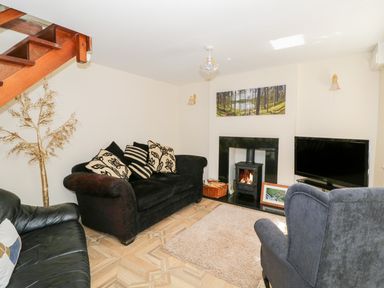 A living room with sofas a fireplace a television and a wooden staircase at Rose Cottage in Bream