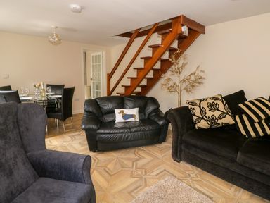 A living room with black leather sofas wooden stairs and a dining table with black chairs at Rose Cottage in Bream