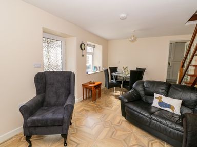 A living room with a black leather sofa a black armchair a glass dining table with four black chairs and wooden stairs at Rose Cottage in Bream
