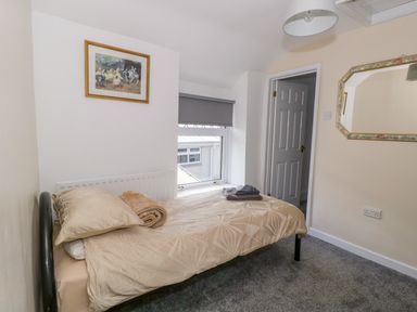 A small bedroom with a single bed pillow blanket and folded towels a window with a blind an open door a framed picture on the wall and a mirror at Rose Cottage in Bream