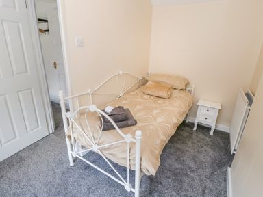 A small bedroom with a single bed covered with beige bedding a white bedside table and grey carpet at Rose Cottage in Bream