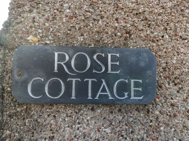 A sign reading Rose Cottage mounted on a rough pebbled wall at Rose Cottage in Bream