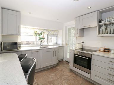 A kitchen with grey cabinets a microwave an oven and two black chairs at Rose Cottage in Bream