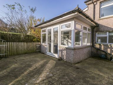 A paved patio area with a wooden fence an attached conservatory with double doors and windows at Rose Cottage in Bream