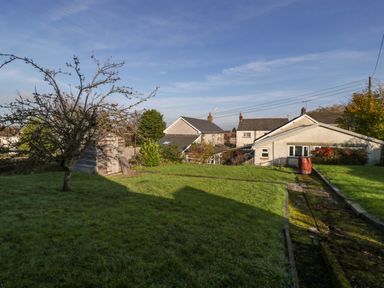 A backyard with grass a tree a wooden shed a paved path and houses in the background at Rose Cottage in Bream