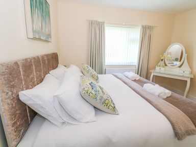 A bedroom with a bed with pillows and rolled towels by a window with curtains and a vanity mirror on a table at Llain Bach in Llangefni