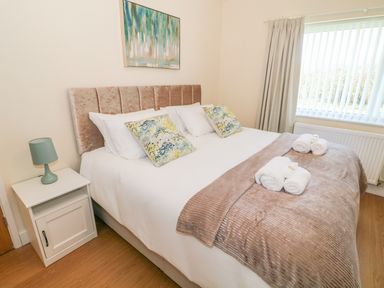 A bedroom with a bed two decorative pillows bedside table with lamp and window with curtains at Llain Bach in Llangefni