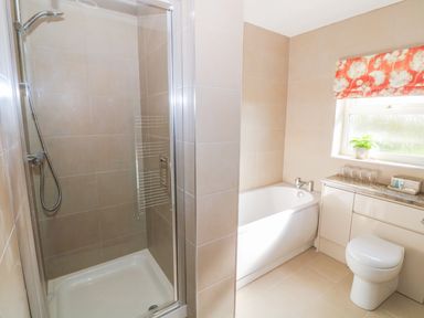 A bathroom with a shower enclosure a bathtub a toilet and a window with a floral blind at Llain Bach in Llangefni