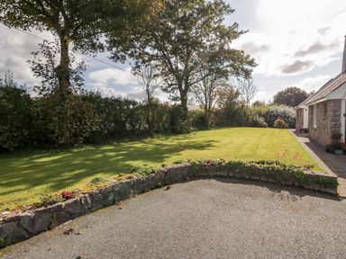 A garden with trees grass and a stone wall next to a stone house at Llain Bach in Llangefni