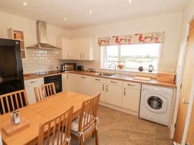 A kitchen with wooden dining table and chairs a washing machine black refrigerator and window with floral valance at Llain Bach in Llangefni