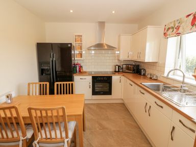 A kitchen with wooden dining table and chairs black refrigerator white cabinets and countertops with sink at Llain Bach in Llangefni