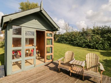 A small wooden garden cabin with two wooden chairs and a table on a wooden deck in a grassy backyard at Llain Bach in Llangefni