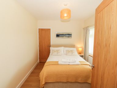 A bedroom with a double bed, bedside table with lamp, wooden doors, and a window with curtains at Llain Bach in Llangefni