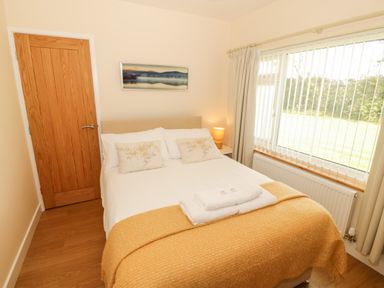 A bedroom with a bed a wooden door and a window with blinds at Llain Bach in Llangefni
