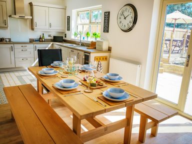 A kitchen and dining area with a wooden table set for six near a glass door leading outside at Oystercatcher in Embleton