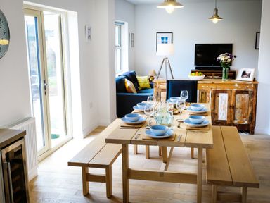 A dining area with a wooden table set with blue bowls and glasses at Oystercatcher in Embleton