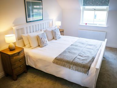 A bedroom with a white bed and bedside tables with lamps at Oystercatcher in Embleton