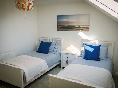 A bedroom with two single beds a bedside table and a wall painting at Oystercatcher Embleton