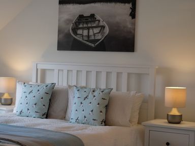 A bedroom with a white bed frame two bedside tables with lamps and decorative pillows on the bed at Oystercatcher in Embleton