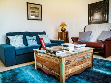 A living room with blue sofa brown armchair and wooden coffee table at Oystercatcher Embleton