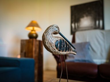 A wooden bird sculpture on a table with a lamp a chair and a wall painting in the background at Oystercatcher in Embleton