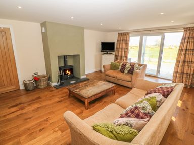 A living room with two sofas and a wooden coffee table near a fireplace and sliding glass doors at Rhos Y Foel Cottage in Nefyn