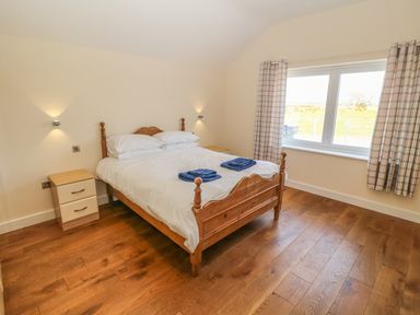 A bedroom with a wooden bed with white bedding two bedside tables and a window with plaid curtains at Rhos Y Foel Cottage in Nefyn