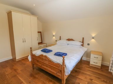 A bedroom with a wooden bed with white bedding and blue towels a wardrobe a bedside table and a dresser with a mirror at Rhos Y Foel Cottage in Nefyn