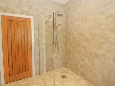 A bathroom with tiled walls and floor a wooden door and a glass walk in shower with a rain showerhead at Rhos Y Foel Cottage in Nefyn