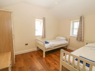 A bedroom with two single beds, wooden floor, a wardrobe, and windows with plaid curtains at Rhos Y Foel Cottage in Nefyn