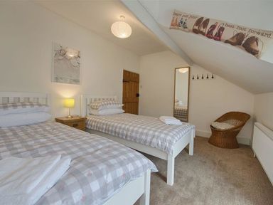 A bedroom with two single beds a bedside table with a lamp a full-length mirror a wicker chair and a wooden door at Anchorage in Watchet